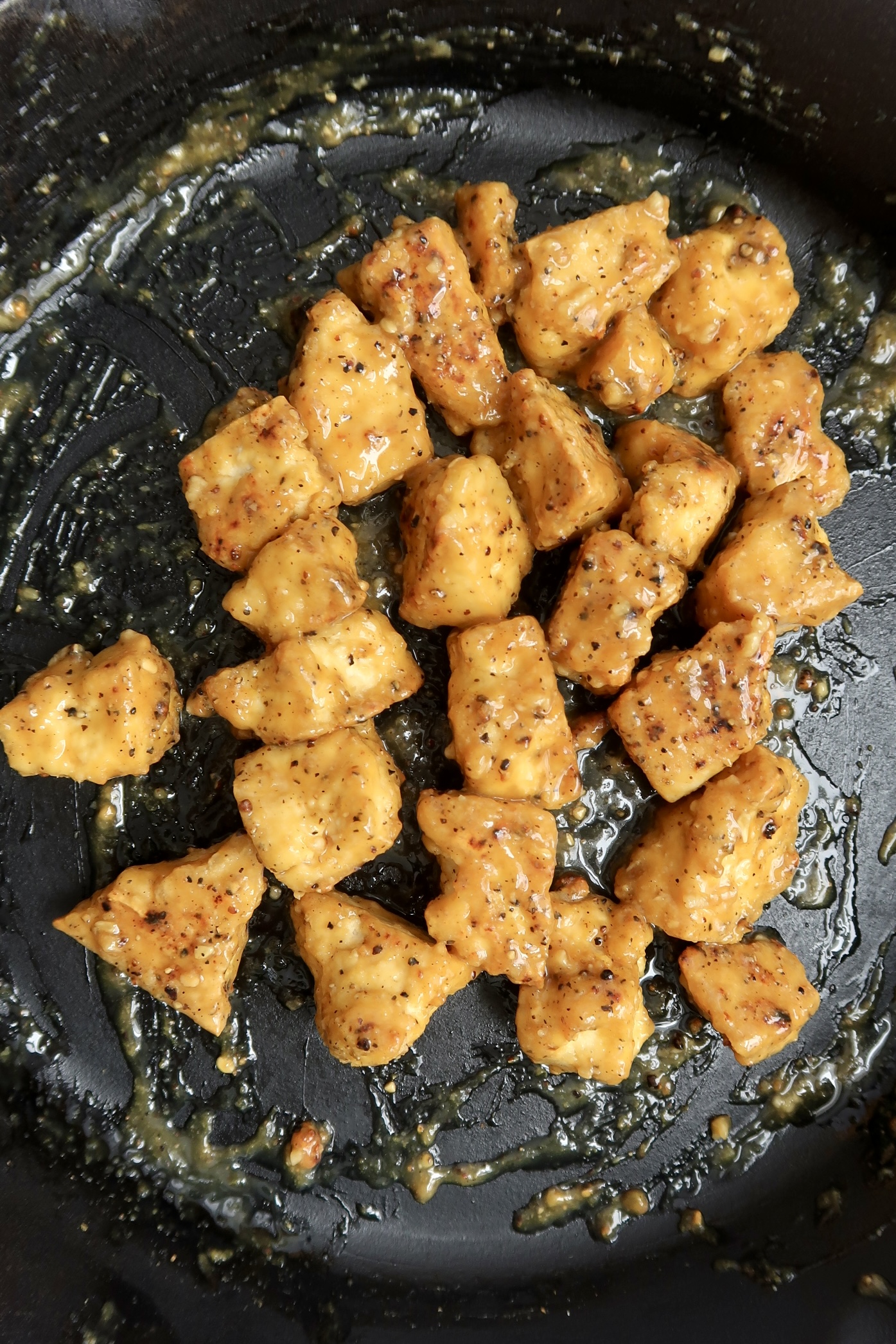 Overhead shot of a cast iron pan with tofu chunks that are cooked in a lemon pepper sauce.