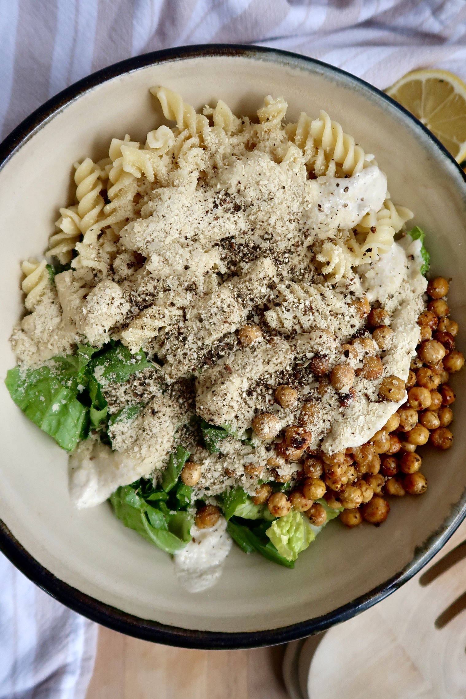Bowl with pasta, romaine lettuce and crispy chickpeas with a creamy dressing and pepper on top.