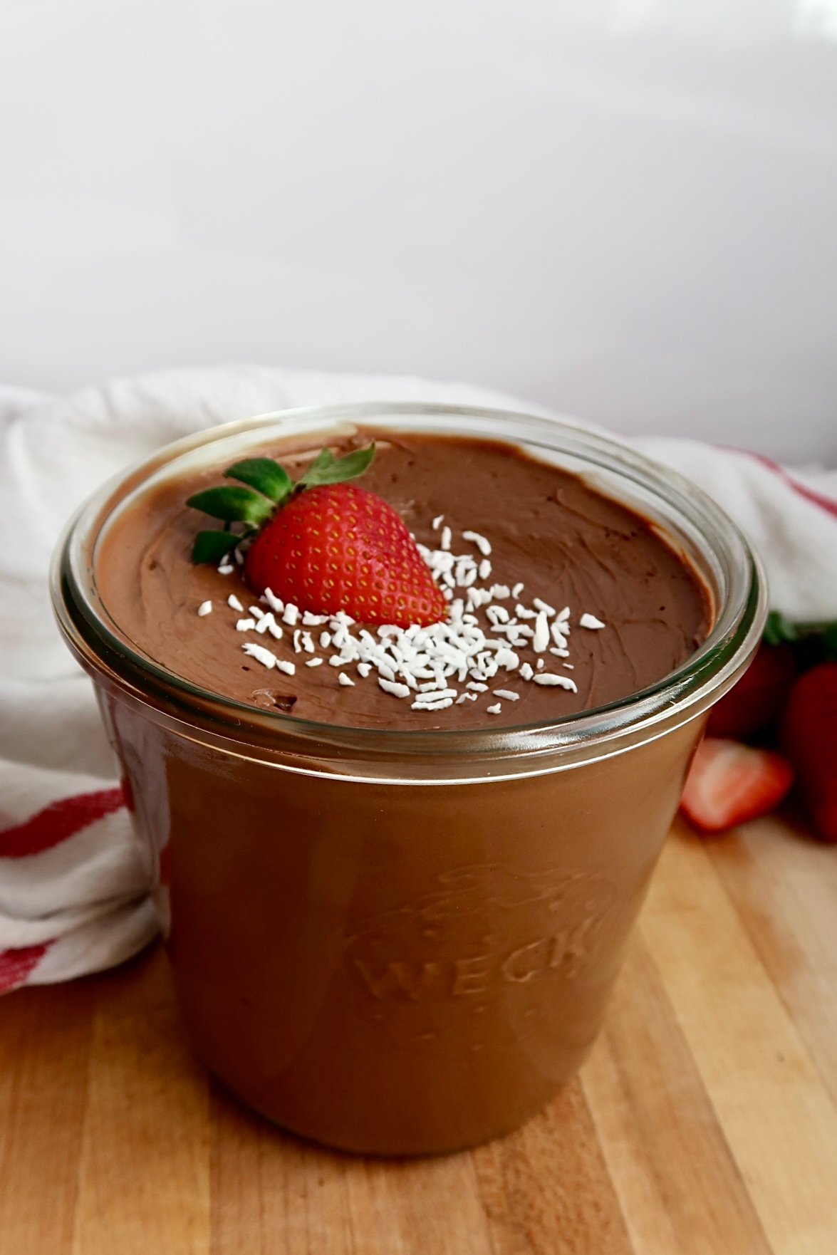 Jar of chocolate mousse with coconut flakes and a strawberry on top.