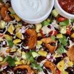 Sheet pan with sweet potato and veggies on top and black beans with salsa and sour cream on the side.