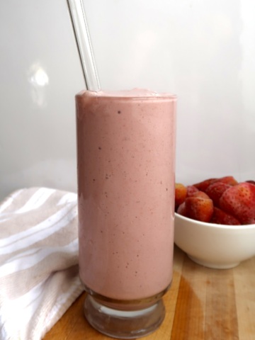 Glass of strawberry smoothie with a bowl of strawberries to the side.