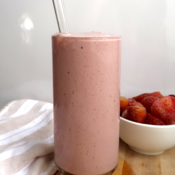 Glass of strawberry smoothie with a bowl of strawberries to the side.