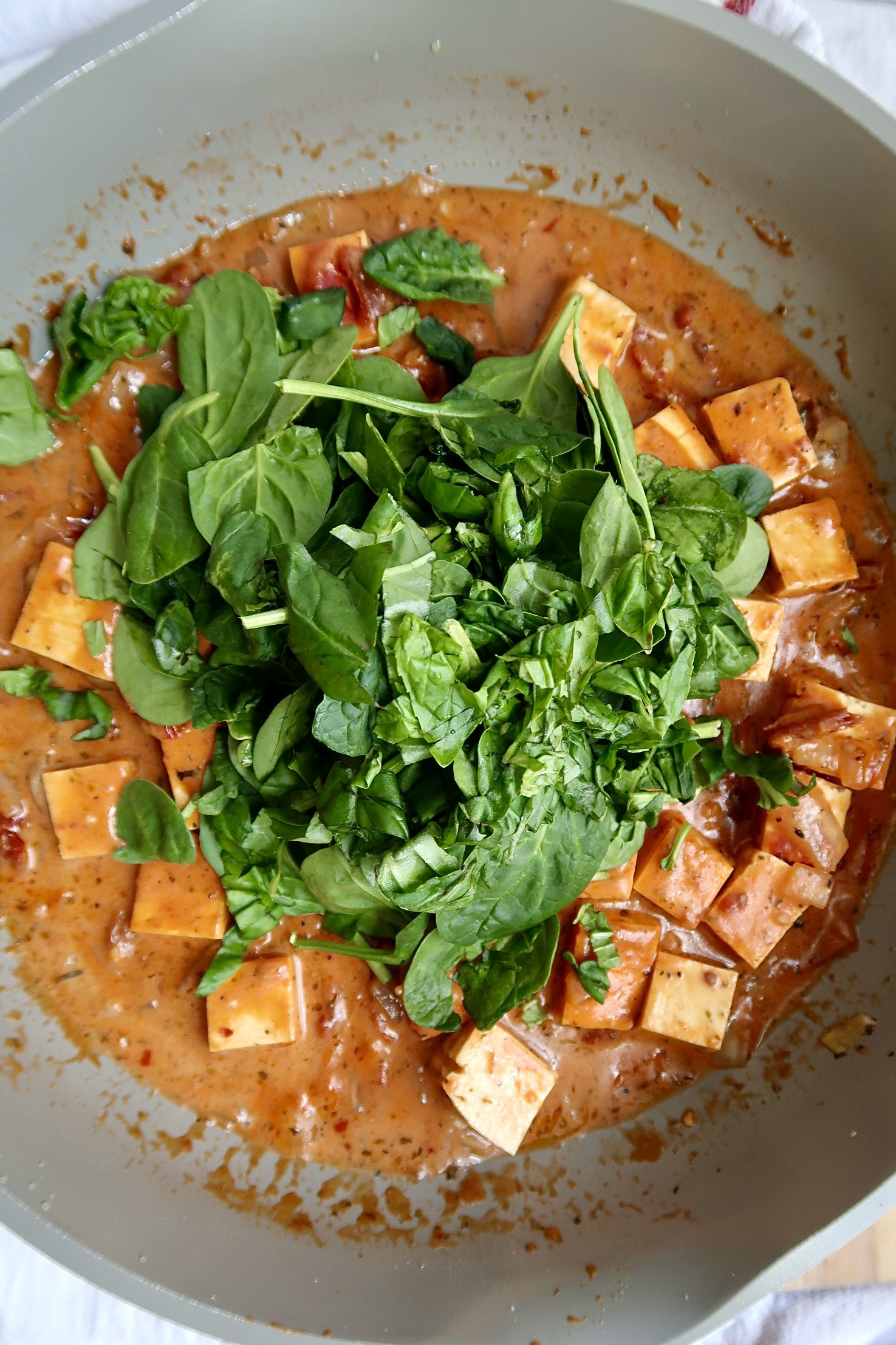 Cubed tofu in a pan with a sauce and spinach over top.