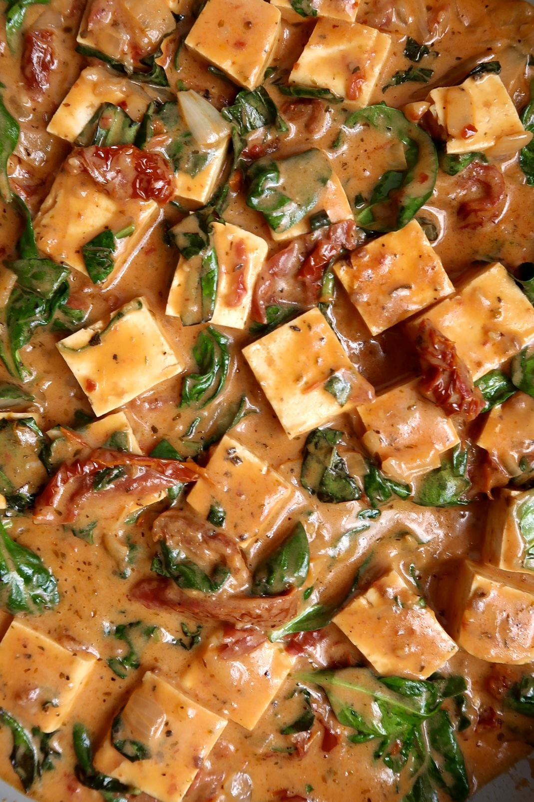Close up of cubed tofu in a pan with a sauce and spinach wilted in.