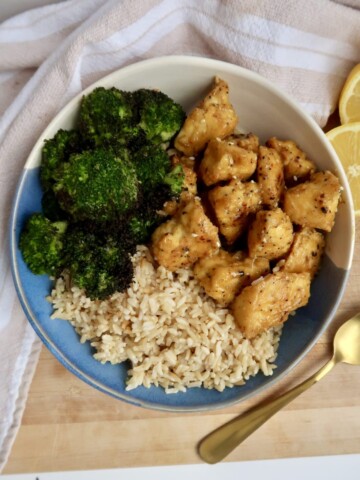 Crispy tofu with a lemon pepper seasoning, brown rice and broccoli in a bowl with a spoon to the side.