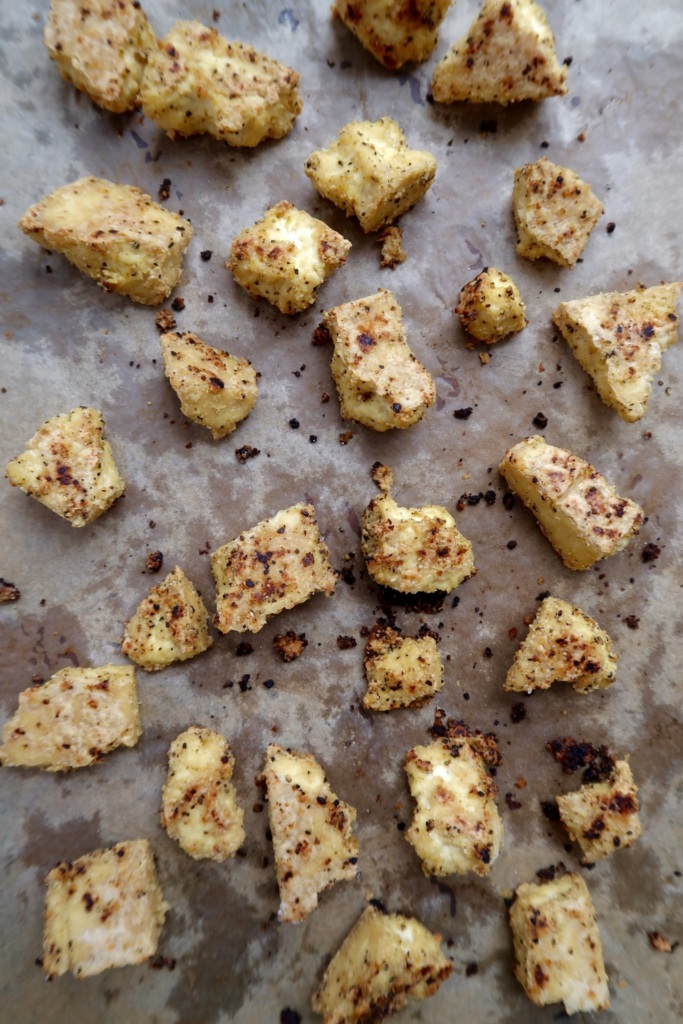 Tofu torn into cubes with seasoning on it on a pan with parchment paper.