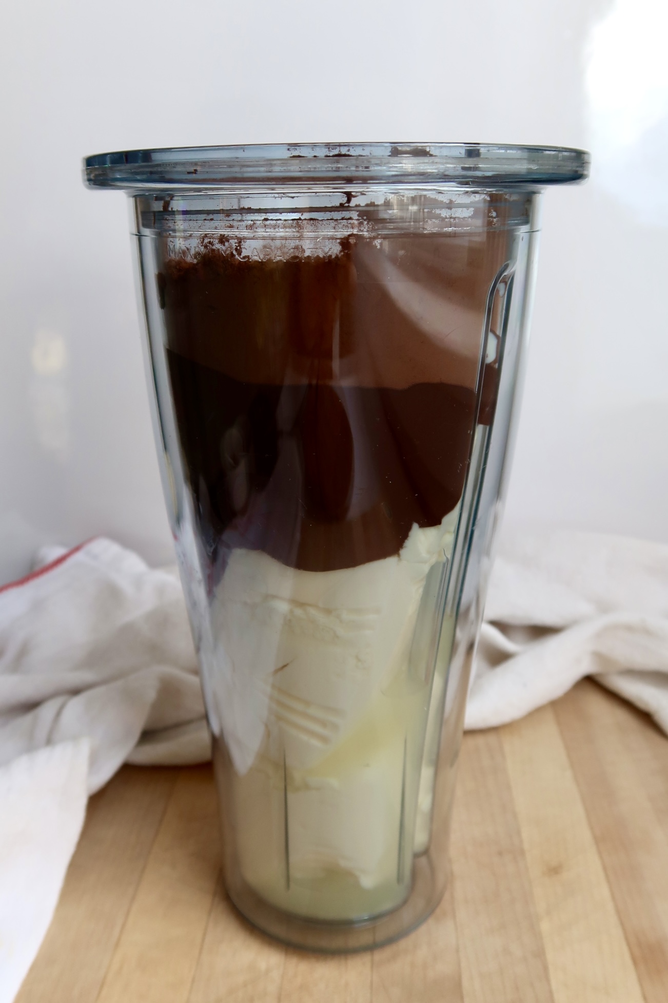 Blender container with silken tofu, melted chocolate and cocoa powder layered in it.