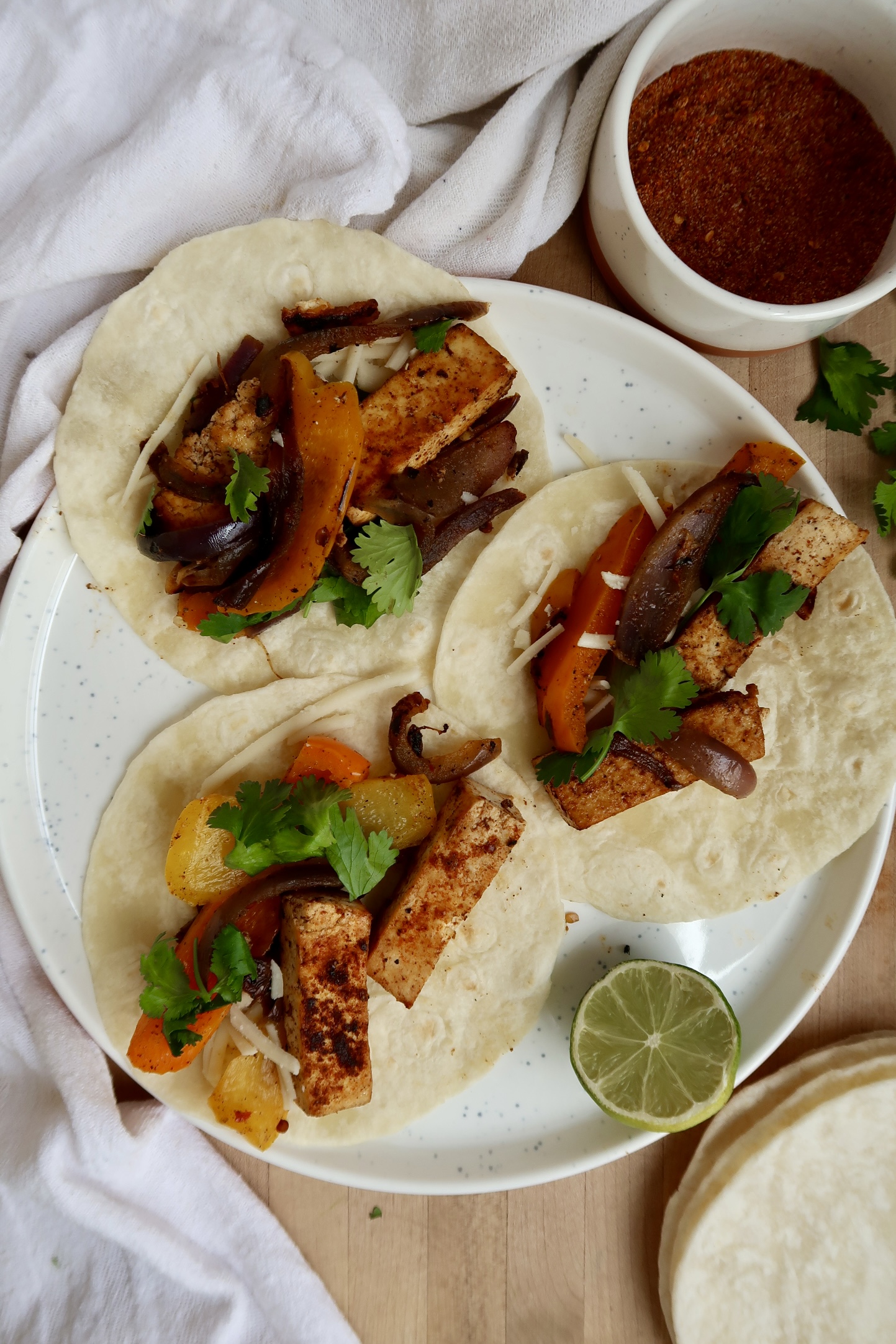 Three tofu fajitas on a plate with salsa to the side.