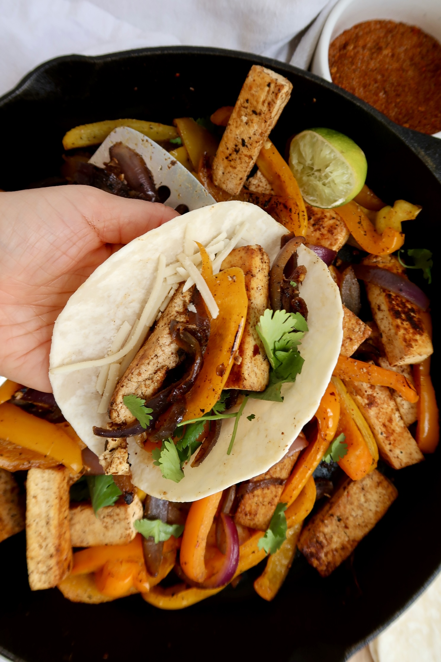 Pan of fajita mix and a hand holding one.