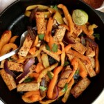 Pan of tofu fajita filling with peppers and a spatula and seasoning mix to the side.