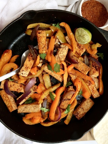 Pan of tofu fajita filling with peppers and a spatula and seasoning mix to the side.