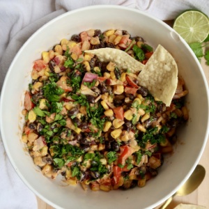 Bowl with black bean and corn salad with chips in it.