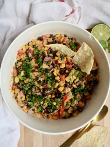 Bowl with black bean and corn salad with chips in it.