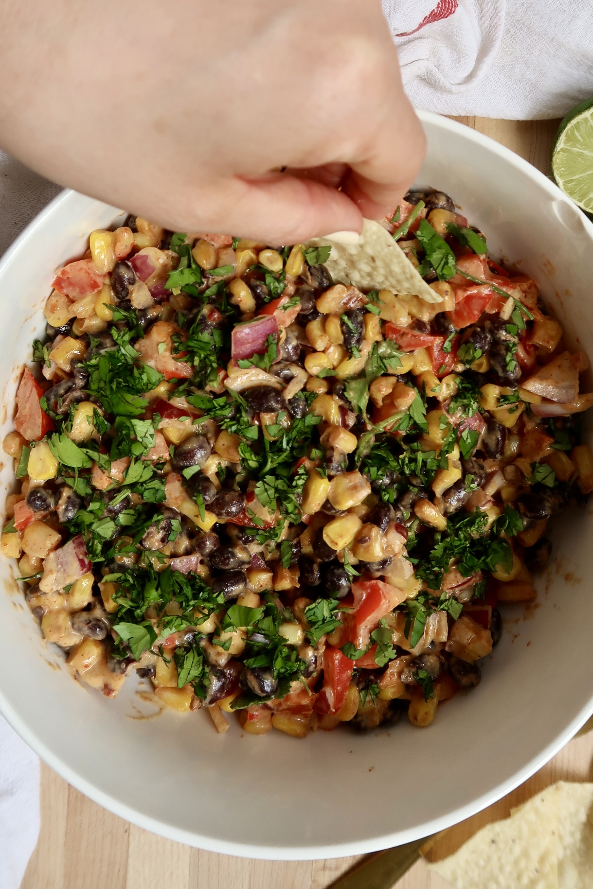 Bowl of black bean and corn salad with hand dipping a chip.