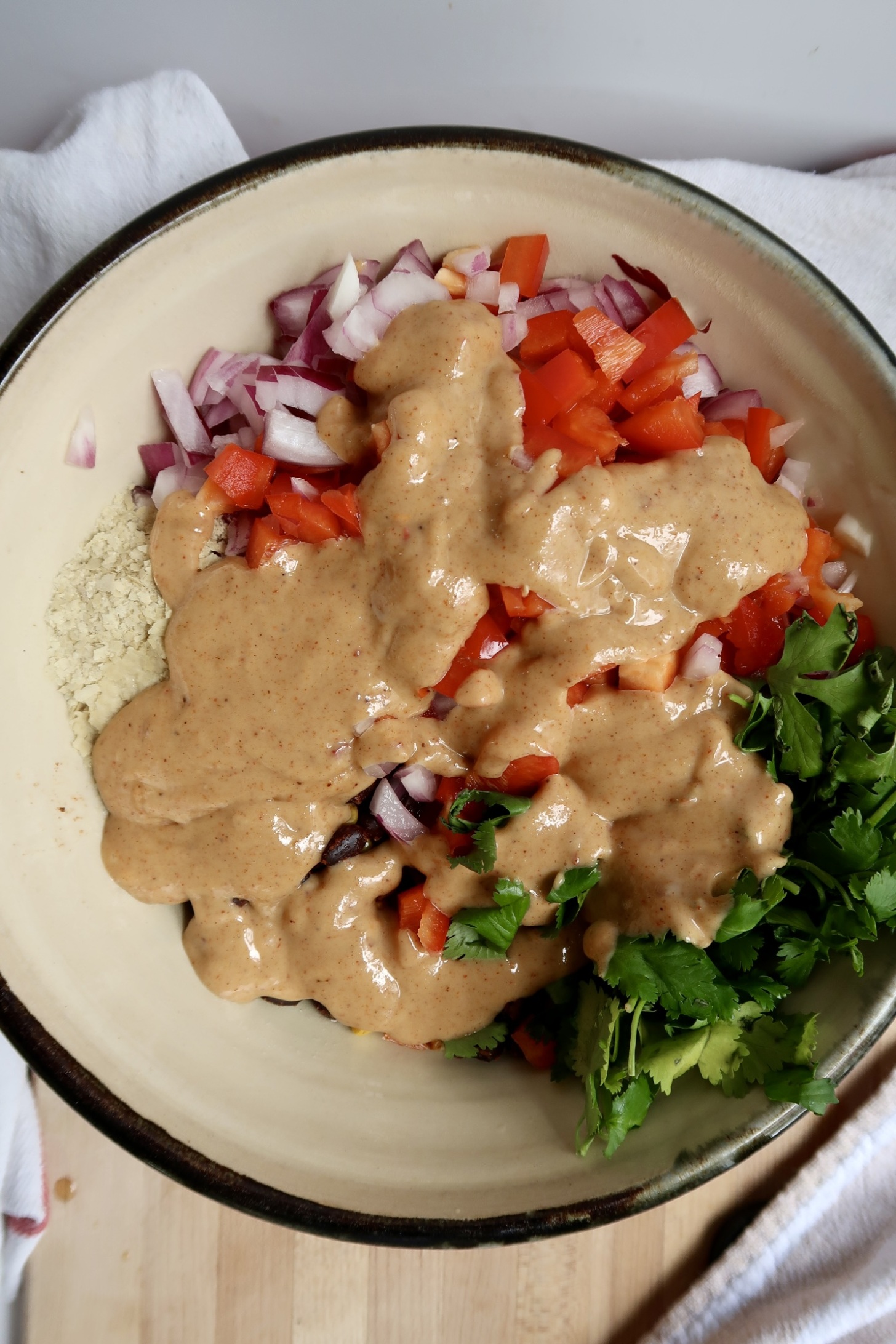 Bowl with bell pepped, red onion, cilantro, nutritional yeast and dressing drizzled on top.