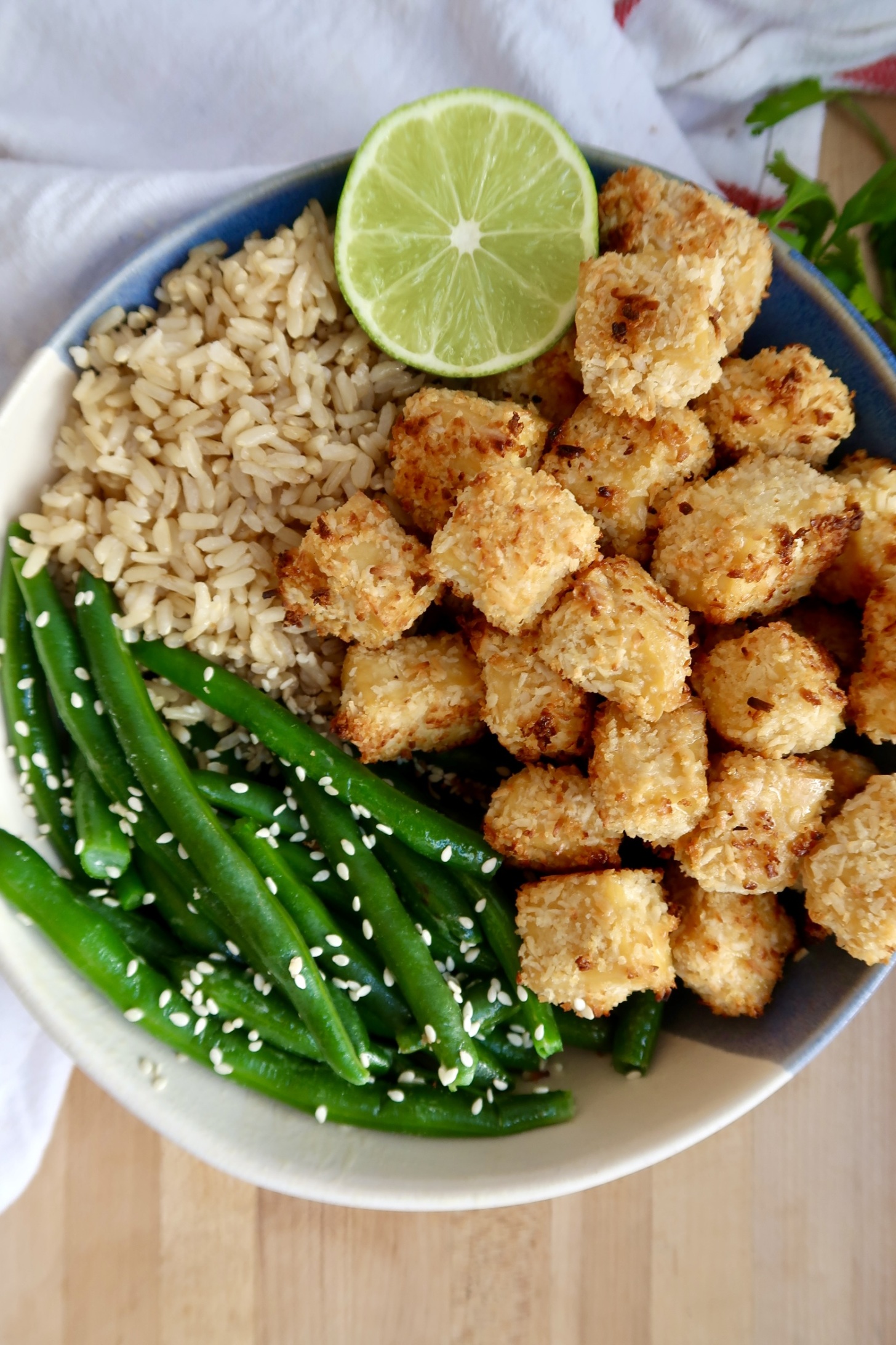 Bowl of coconut crusted tofu with green beans, rice and lime to the side.