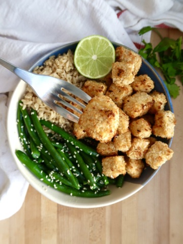 Bowl of coconut tofu with green beans, rice and lime to the side and a fork with a piece of tofu.