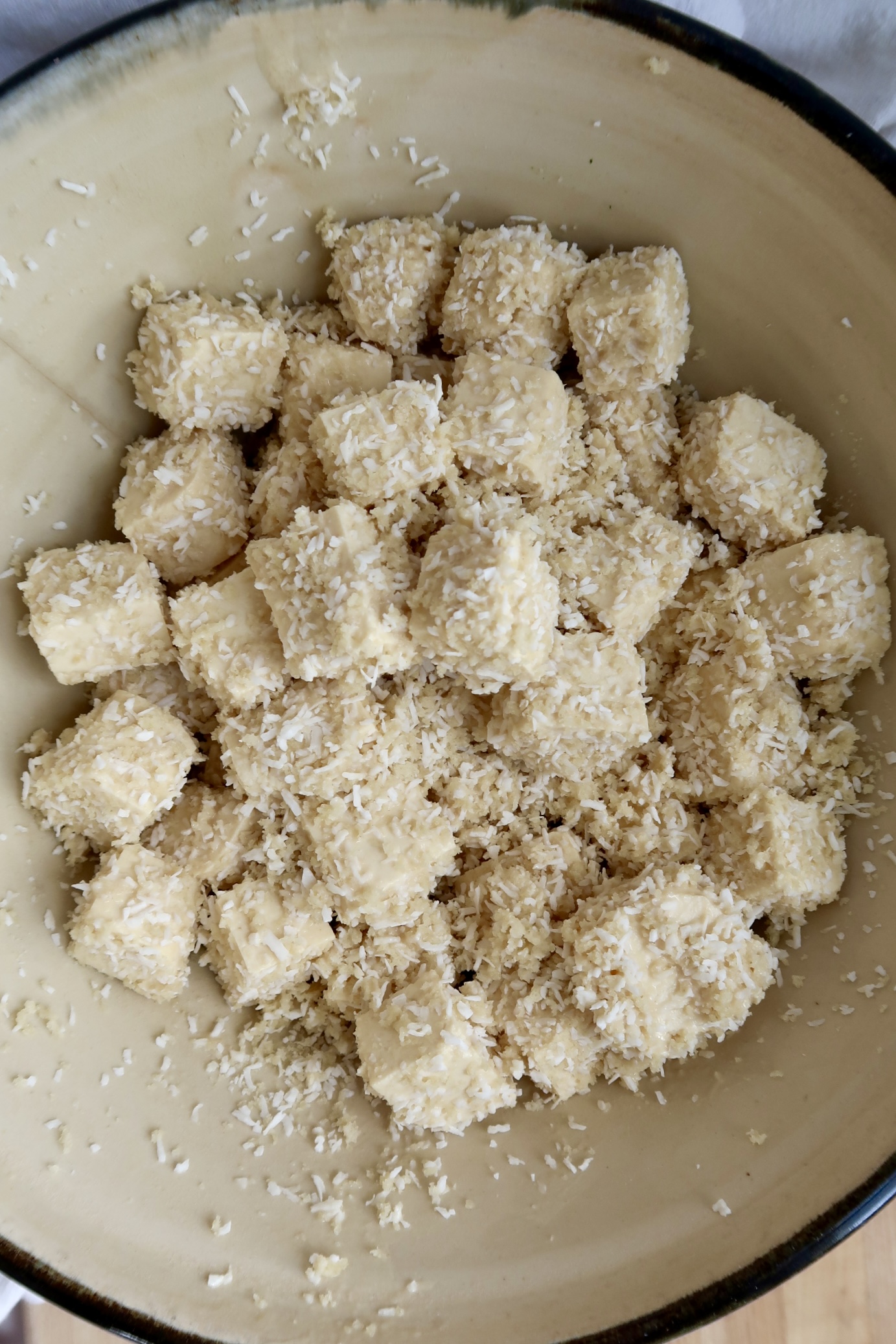 Bowl of cubed tofu with coconut flakes and bread crumbs on it.
