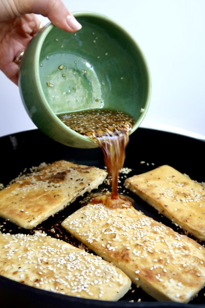 Pan of ginger sesame tofu cooking with sauce being poured over top.