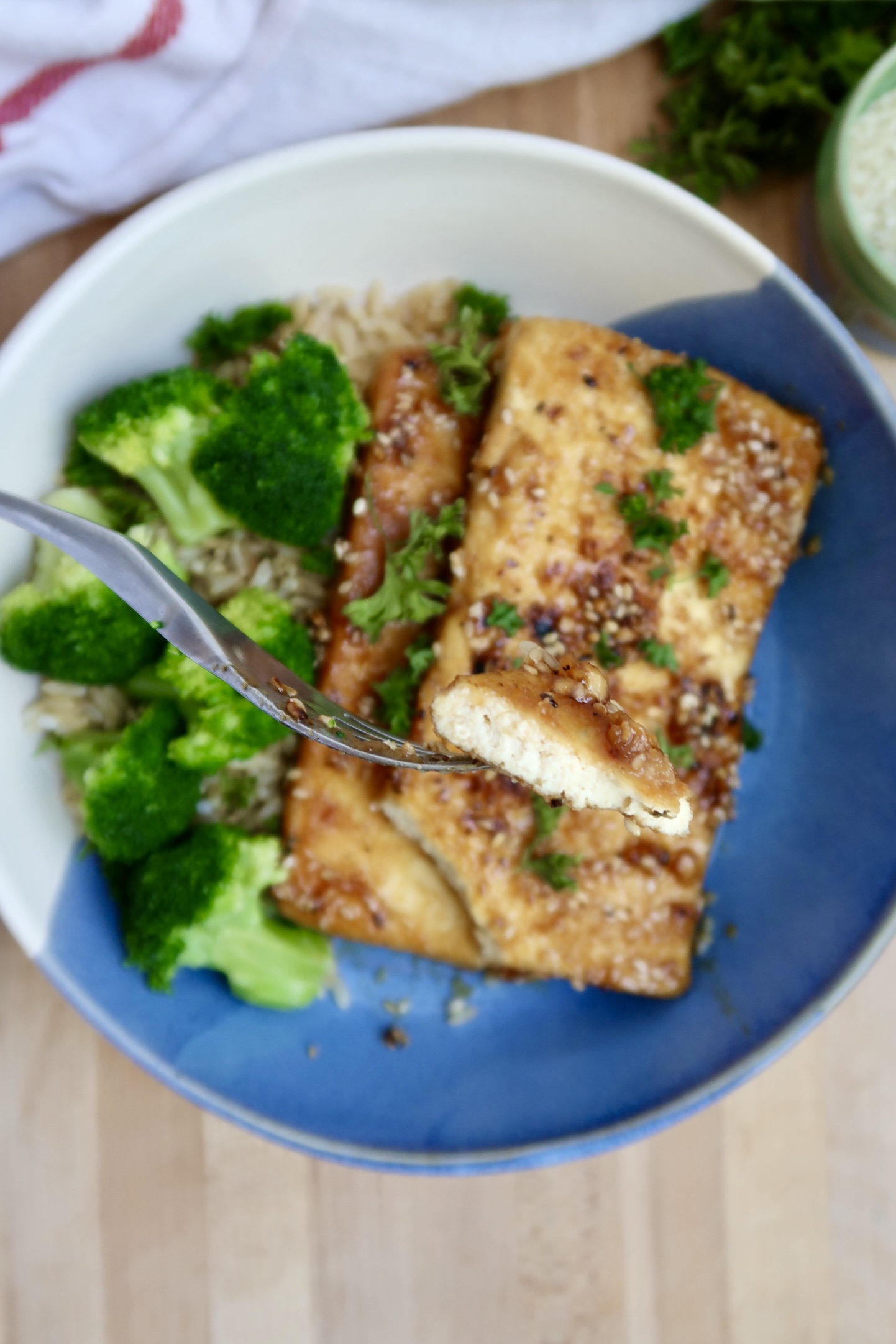 Bowl of ginger sesame tofu with broccoli and a fork with a piece cutting the tofu.