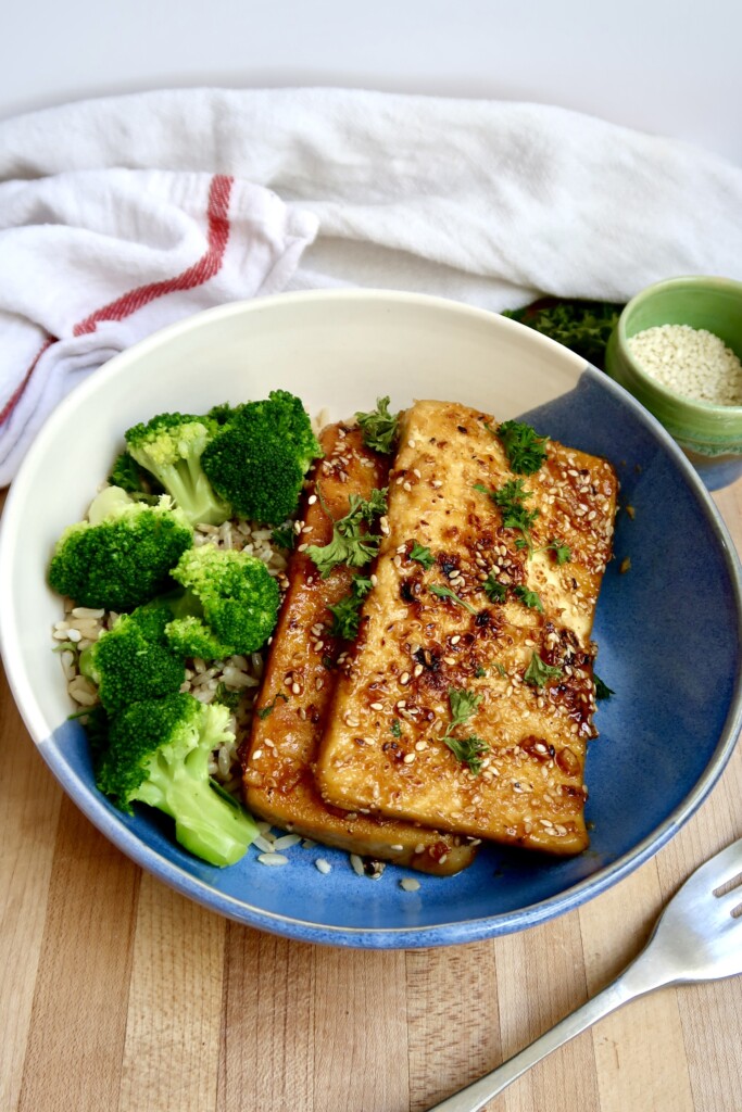 Bowl with two pieces of ginger sesame tofu with rice and broccoli.