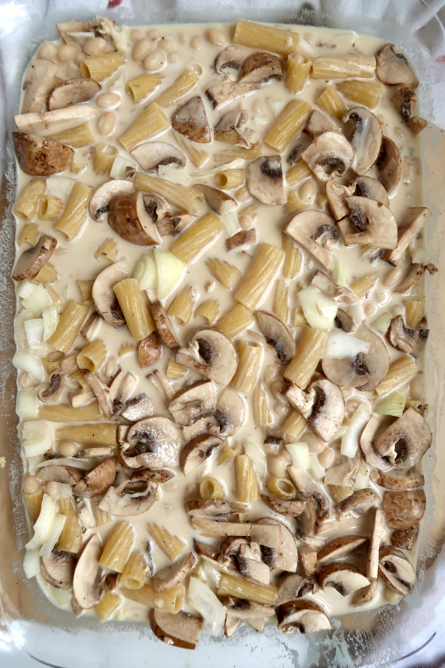 Casserole dish with pasta, mushrooms, diced onion and a creamy sauce.