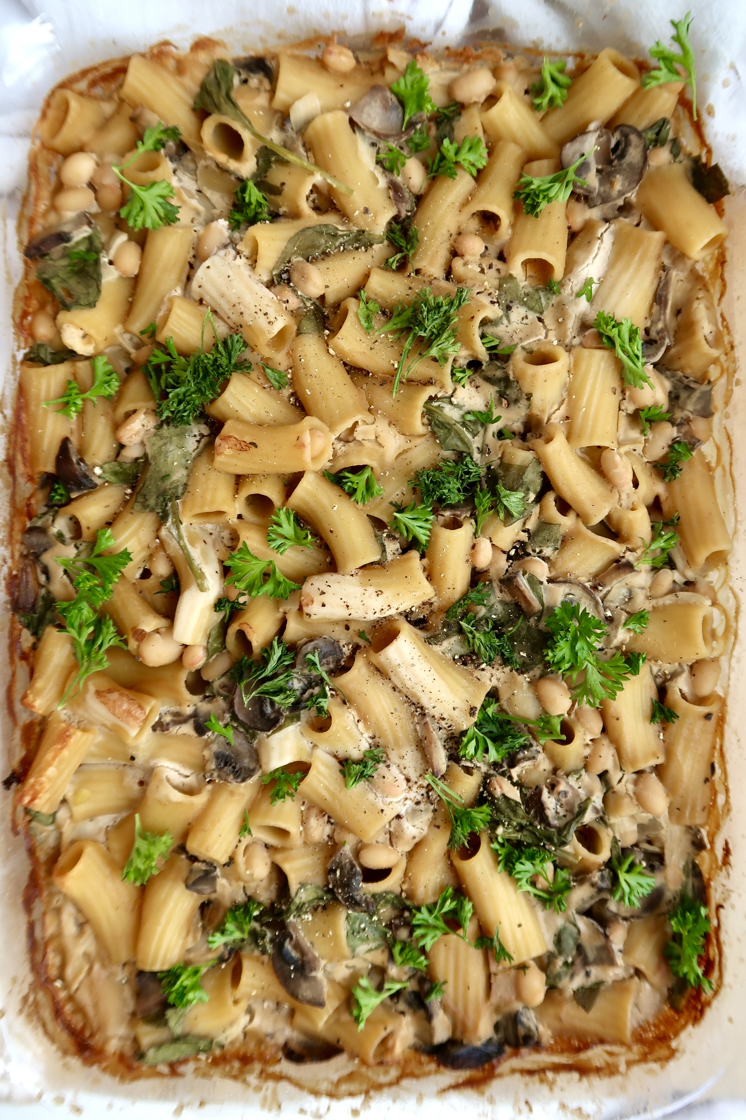 Cooked pasta in a casserole dish with mushroom and parsley on top.