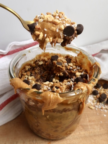 Side shot of spoon scooping overnight oats with peanuts and chocolate chips in it.