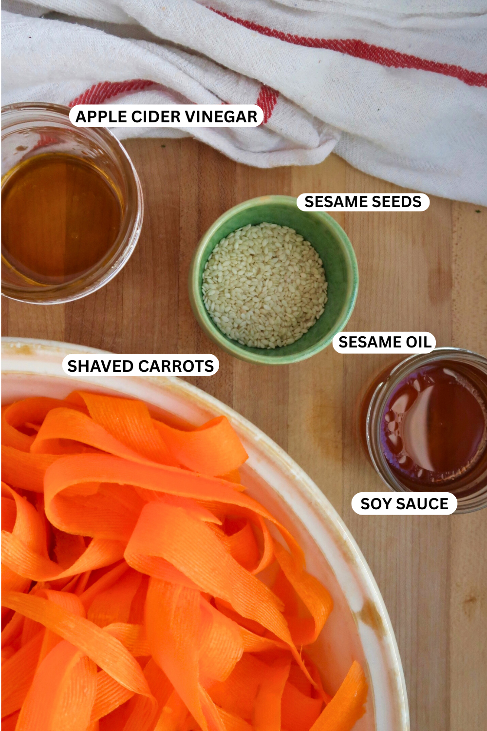 Ingredient flatlay of shaved carrot, soy sauce, sesame oil, sesame seeds and apple cider vinegar.
