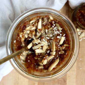 Overnight oats in a jar with date paste, coconut flakes and almonds slives on top and spoon.
