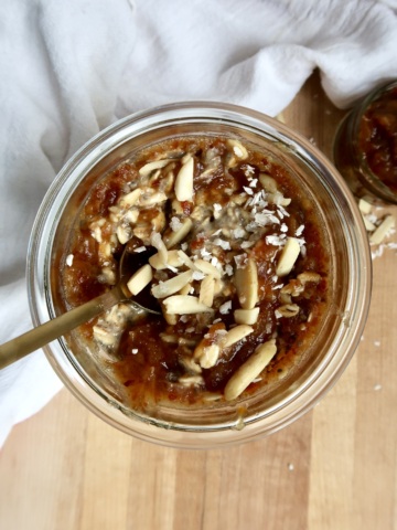 Overnight oats in a jar with date paste, coconut flakes and almonds slives on top and spoon.