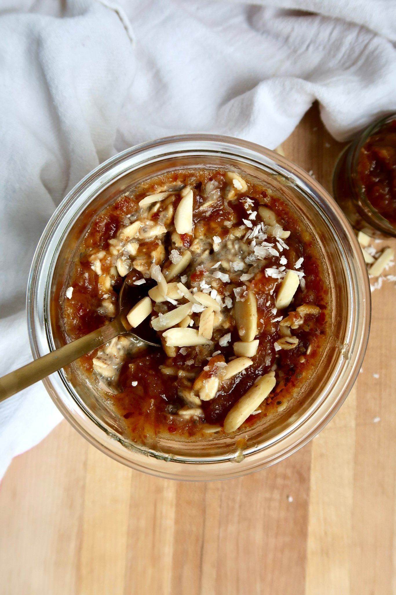 Overnight oats in a jar with date paste, coconut flakes and almonds slives on top and spoon.