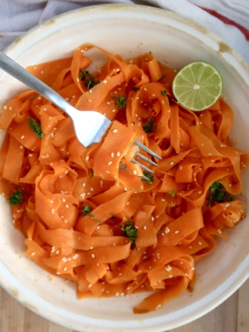 Shaved carrots with sesame seeds, parsley and lime with a fork spiraling some.