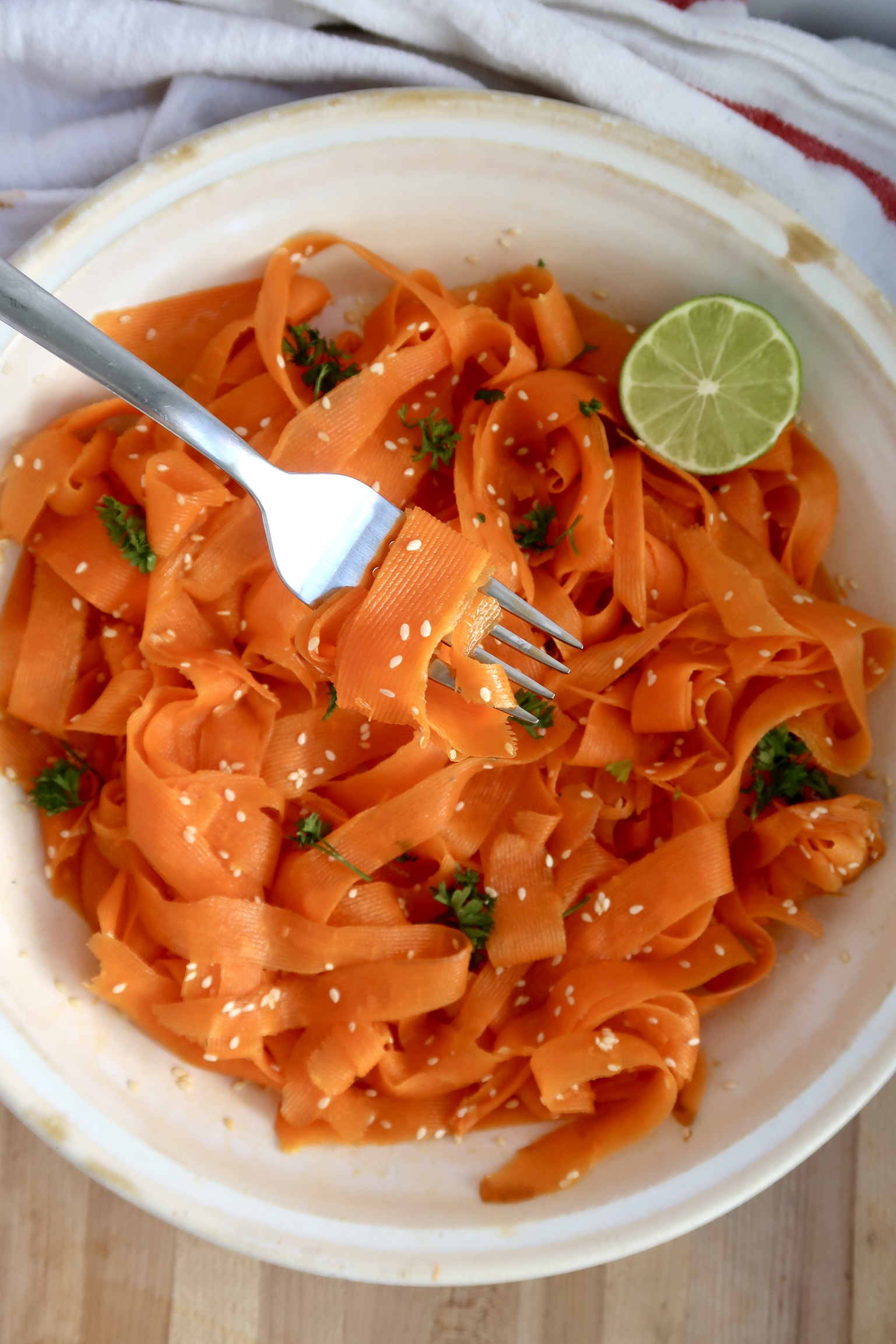 Shaved carrots with sesame seeds, parsley and lime with a fork spiraling some.