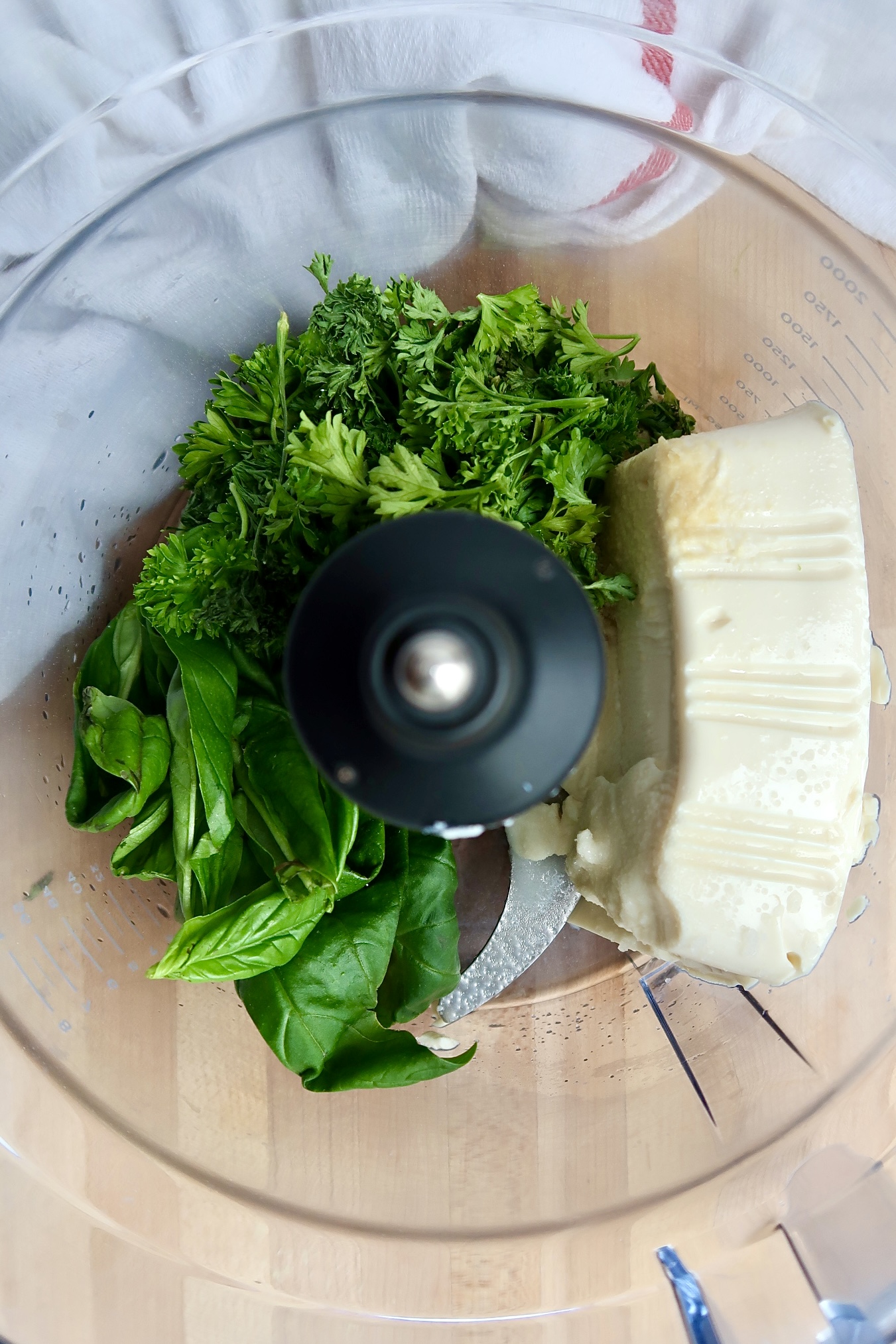 Food processor with tofu, parsley and basil inside.