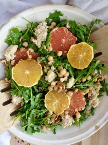 Arugula salad with citrus on top and ricotta and chickpeas with salad tongs inside.