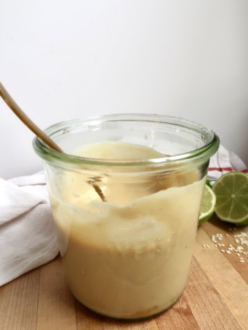 Side view of jar with creamy ginger dressing inside and a spoon.