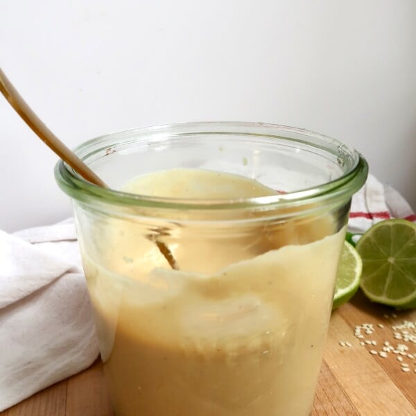 Side view of jar with creamy ginger dressing inside and a spoon.
