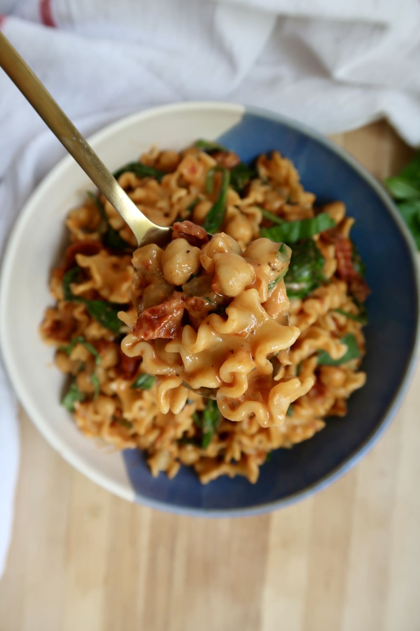 Bowl with pasta in it with spinach, sundried tomatoes and chickpeas with a spoon in it.