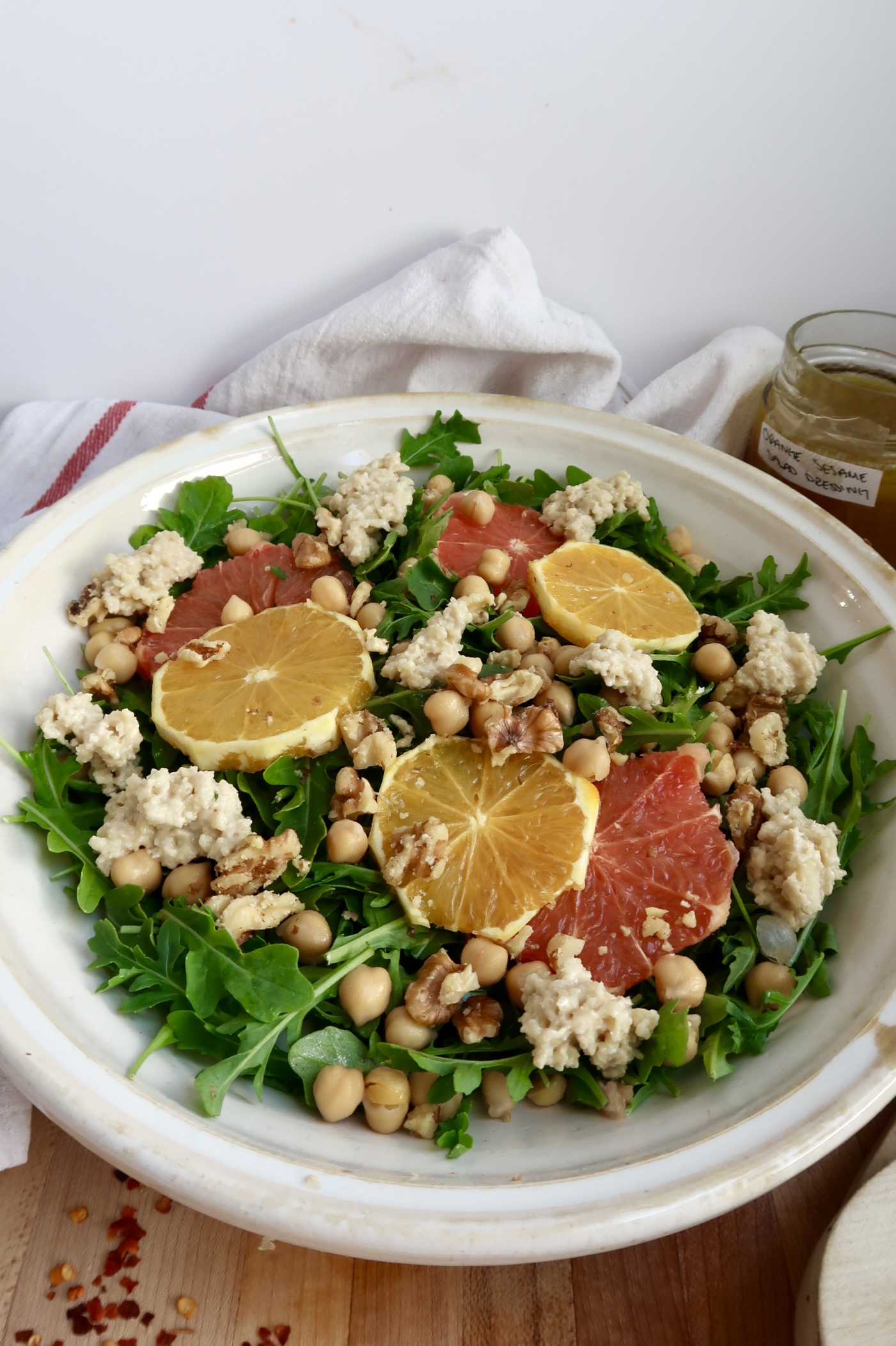Arugula salad with citrus on top and ricotta and chickpeas and salad dressing to the side.