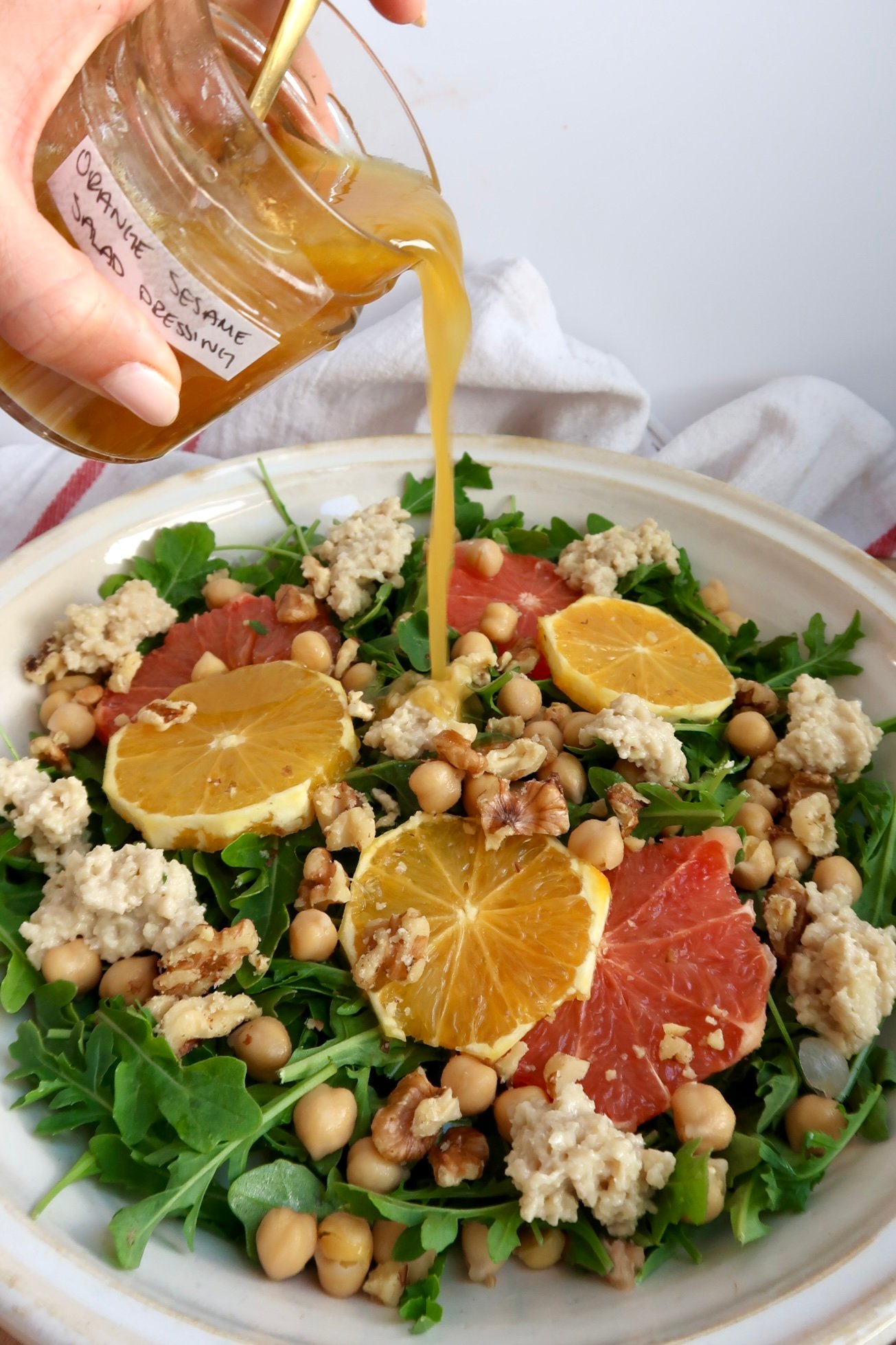 Arugula salad with citrus on top and ricotta and chickpeas and salad dressing being poured on top. 