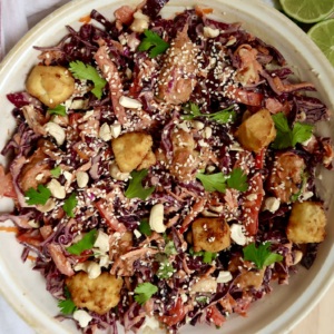 Colorful salad with red cabbage, tofu cubes, cilantro, and a creamy sesame ginger dressing in a white bowl.