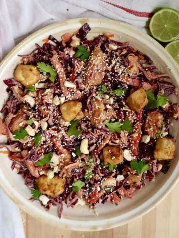Colorful salad with red cabbage, tofu cubes, cilantro, and a creamy sesame ginger dressing in a white bowl.