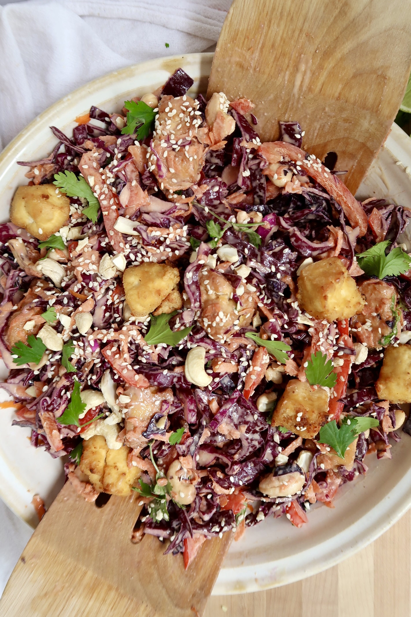 Overhead view of a vibrant cabbage salad tossed with tofu, sesame seeds, red pepper, and a creamy dressing.