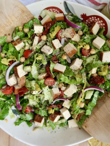 Bowl with salad with tofu, cherry tomatoes, chickpeas, red onion, sundried tomatoes mixed in.