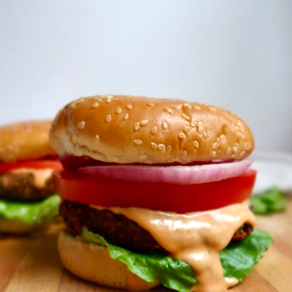 Black bean burger topped with lettuce, tomato, onion, and a generous drizzle of sauce on a sesame bun.