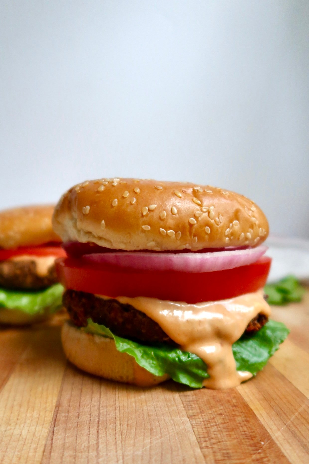 Black bean burger topped with lettuce, tomato, onion, and a generous drizzle of sauce on a sesame bun.