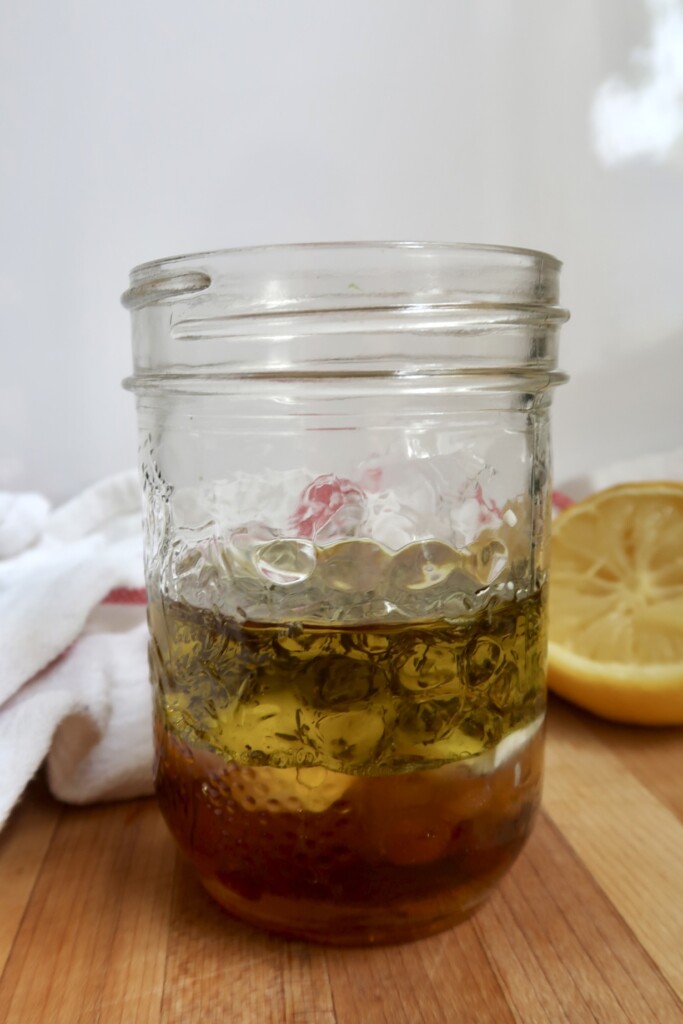 Jar filled with olive oil, dried herbs, and seasonings before mixing