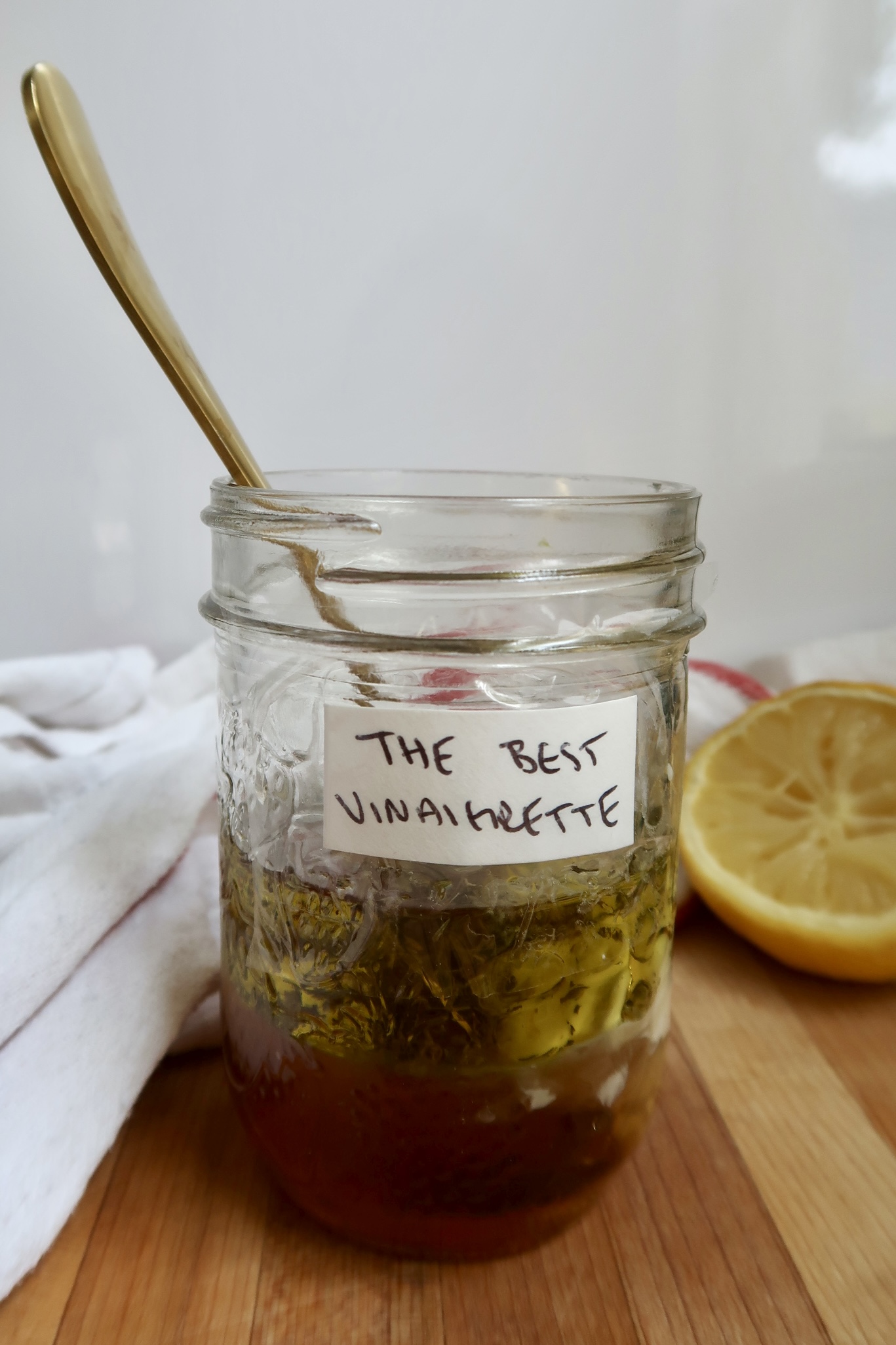 Jar of vinaigrette with olive oil and lemon in the background.