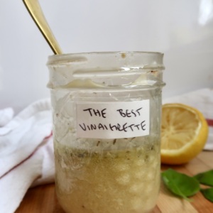 Stirring the vinaigrette in the jar using a golden spoon on a wooden board